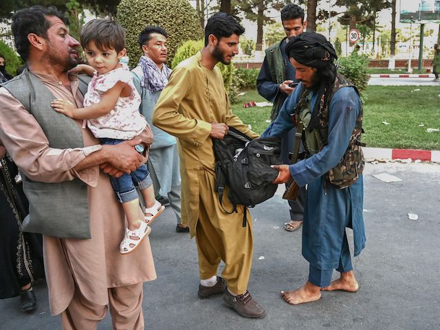 A Taliban fighter (R) searches the bags of people coming out of the Kabul airport in Kabul on August 16, 2021, after a stunningly swift end to Afghanistan's 20-year war, as thousands of people mobbed the city's airport trying to flee the group's feared hardline brand of Islamist rule. (Photo by Wakil Kohsar / AFP) (Photo by WAKIL KOHSAR/AFP via Getty Images)